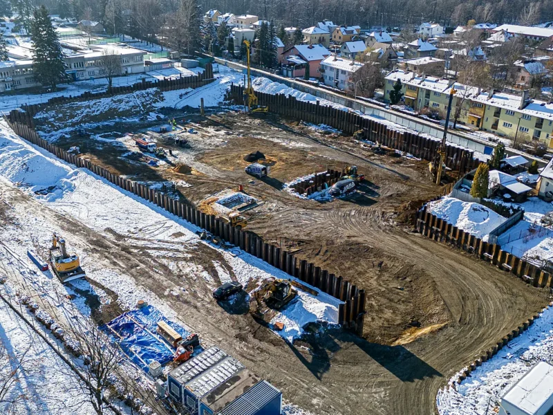 Aerial view of an excavation pit with a sheet pile wall, snow-covered surroundings and blocks of flats