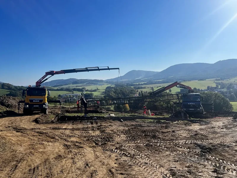 Nákladné vozidlo MAN 6×6 s hydraulickou rukou HIAB pri montáži na stavbe, v pozadí kopce