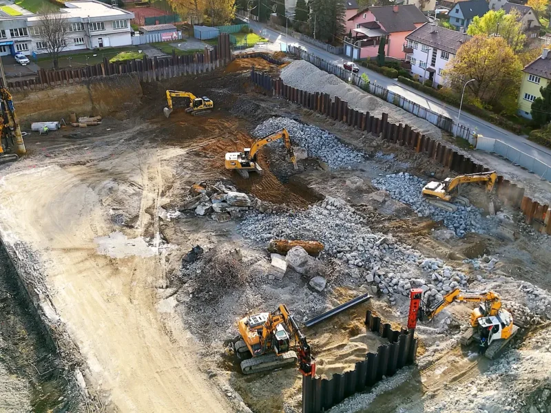View from above onto the bottom of an excavation pit, excavators at work and a sheet pile wall around the perimeter