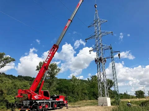 Červený autožeriav ENZA pri stožiari vedenia VN, na konštrukcii pracujú montéri