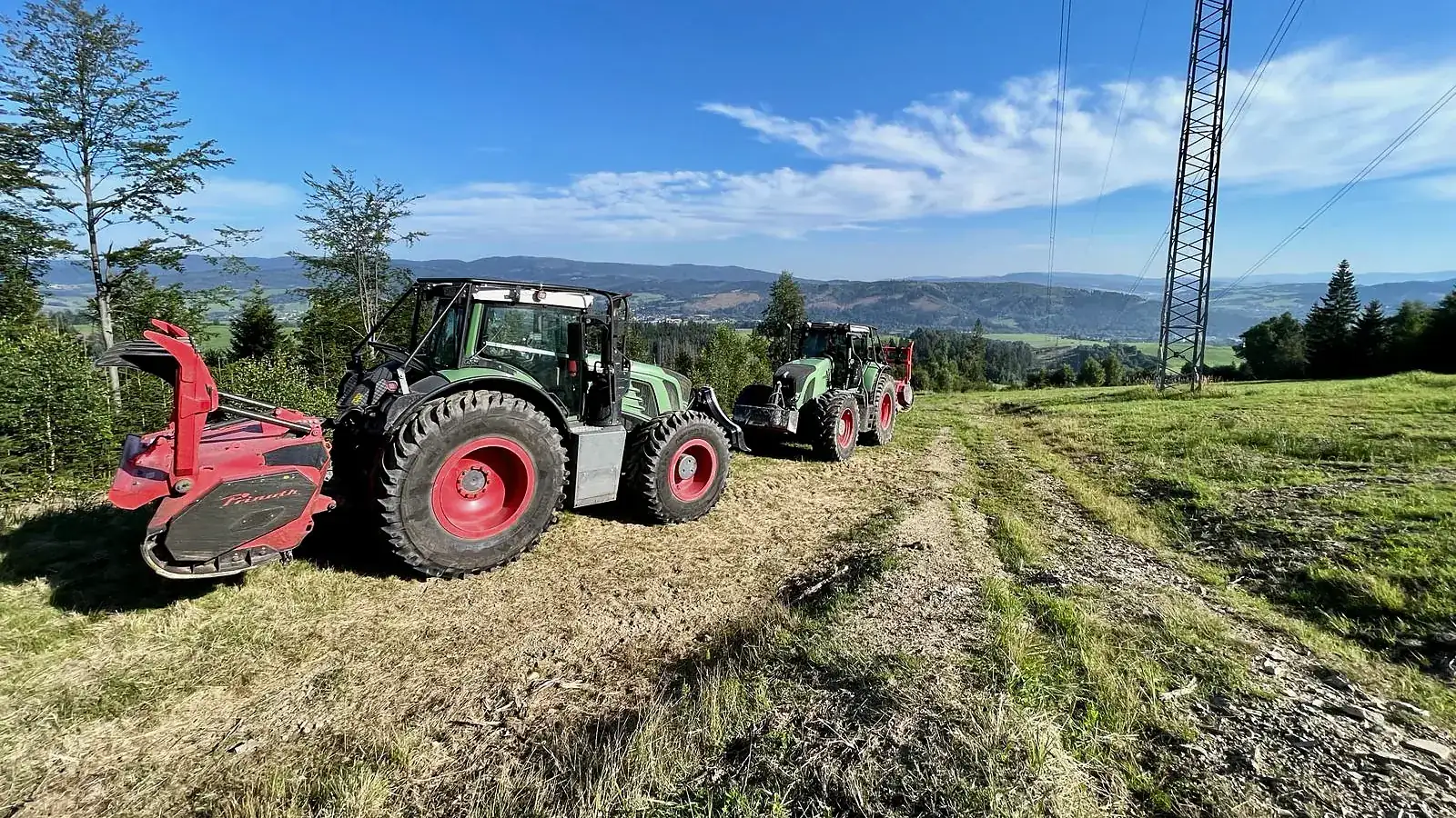 Traktor Fendt s mulčovačom na lúke pod vedením vysokého napätia, v pozadí kopce