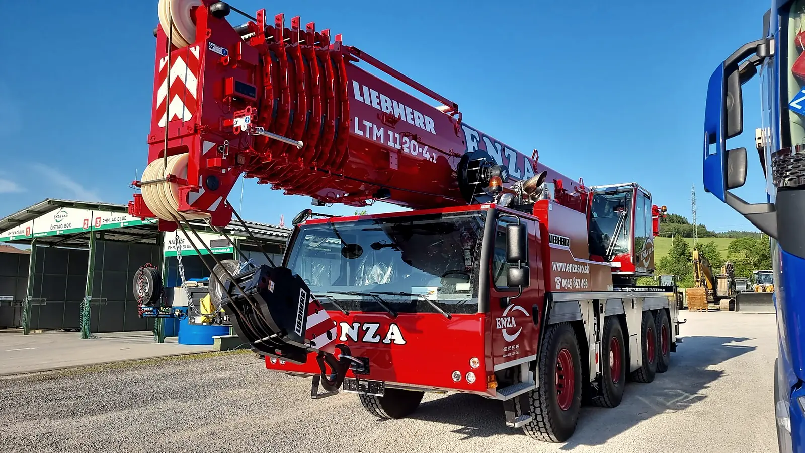Červený autožeriav Liebherr LTM 1120-4.1 s nápisom ENZA na štrkovom areáli