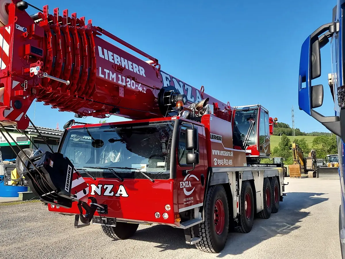 Červený autožeriav Liebherr LTM 1120-4.1 s nápisom ENZA na štrkovom areáli